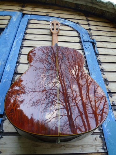 Modelo Orfeo, Guitarras Calliope, Rückseite, hängt an der abgebeizten Tür eines alten hölzernen Zirkuswagens. Bäume, noch ohne Blätter,spiegeln sich auf der Gitarren_Rückseite